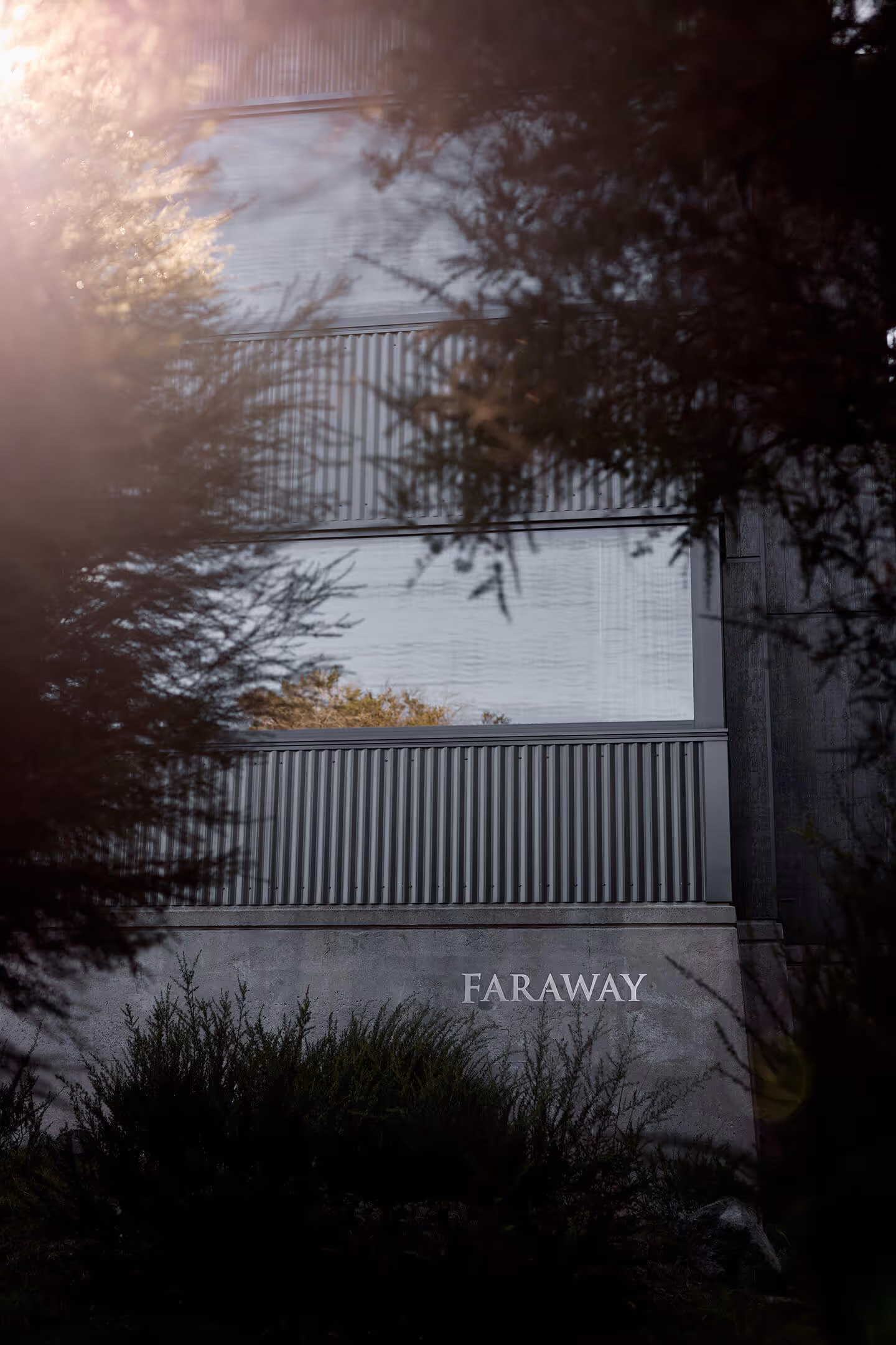 Modern building facade with metal panels and the word FARAWAY on a concrete wall surrounded by bushes.