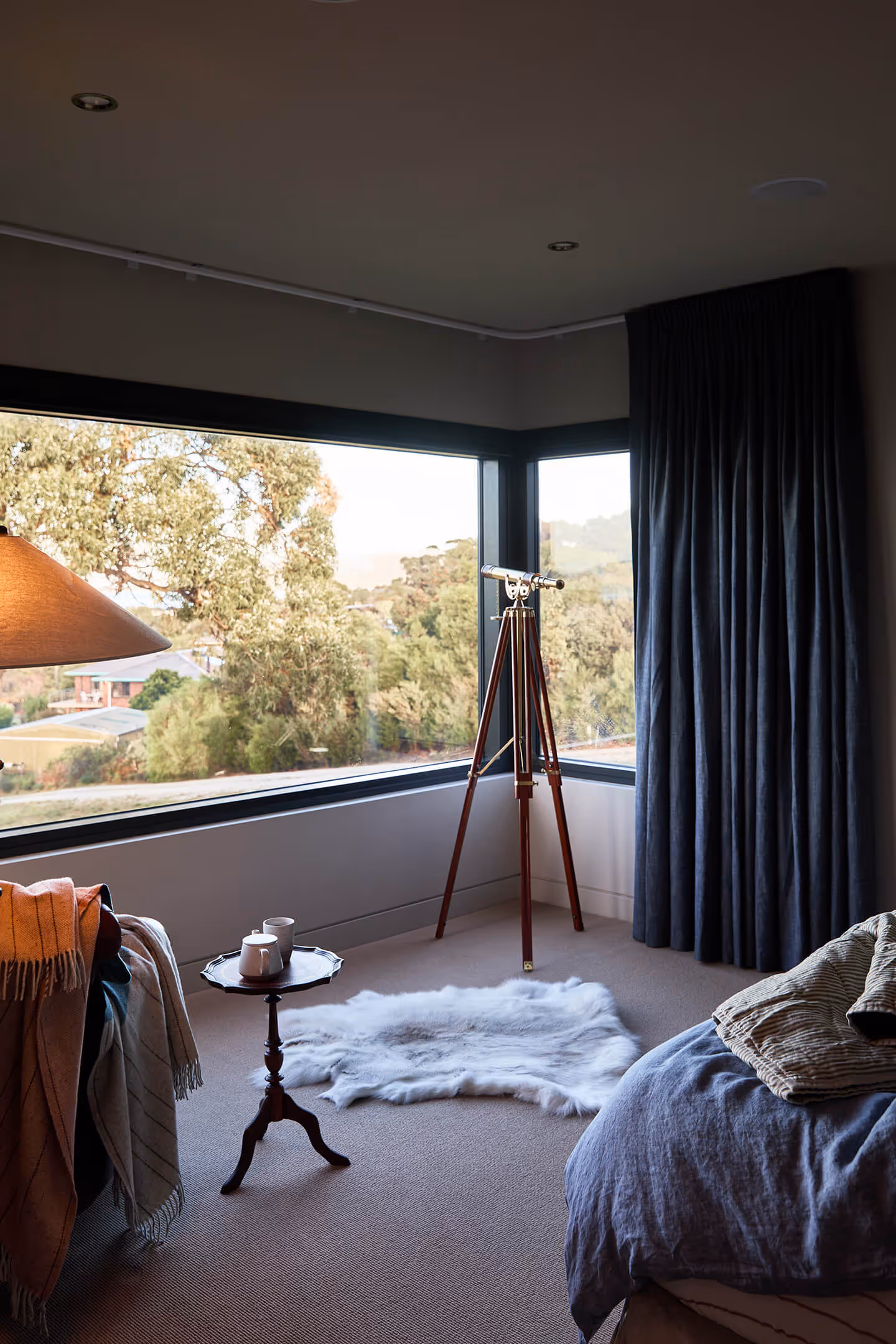 Cozy bedroom corner with telescope by large windows, small table with cups, and a faux fur rug on carpet.
