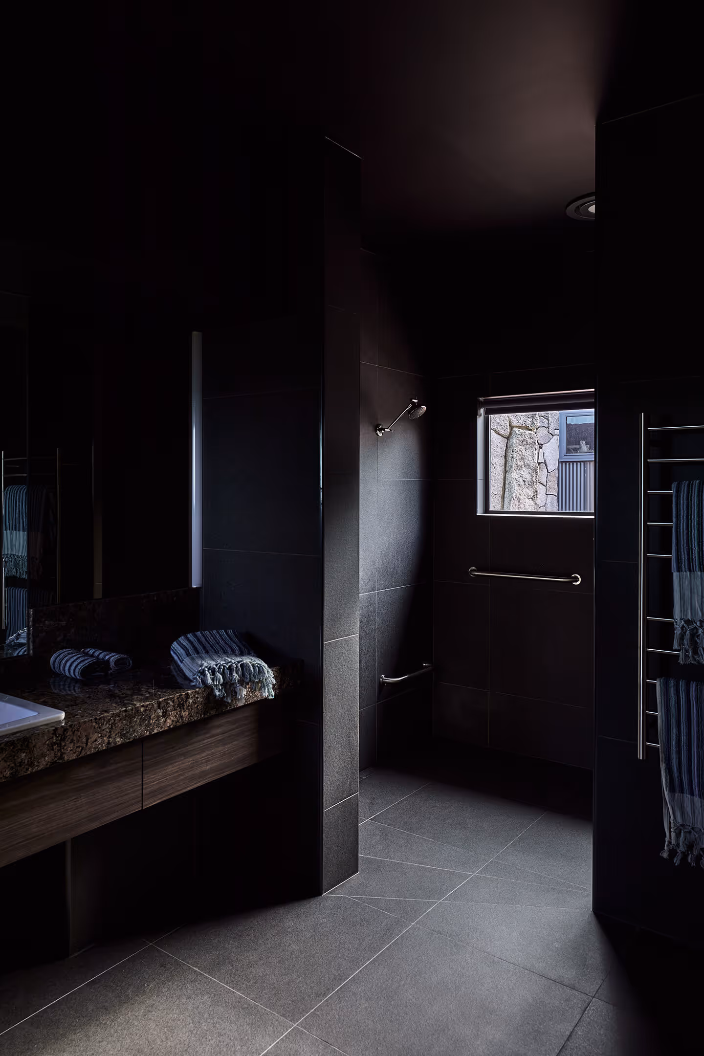 Dark modern bathroom with tiled floors, a window, striped towels, and a stone countertop.