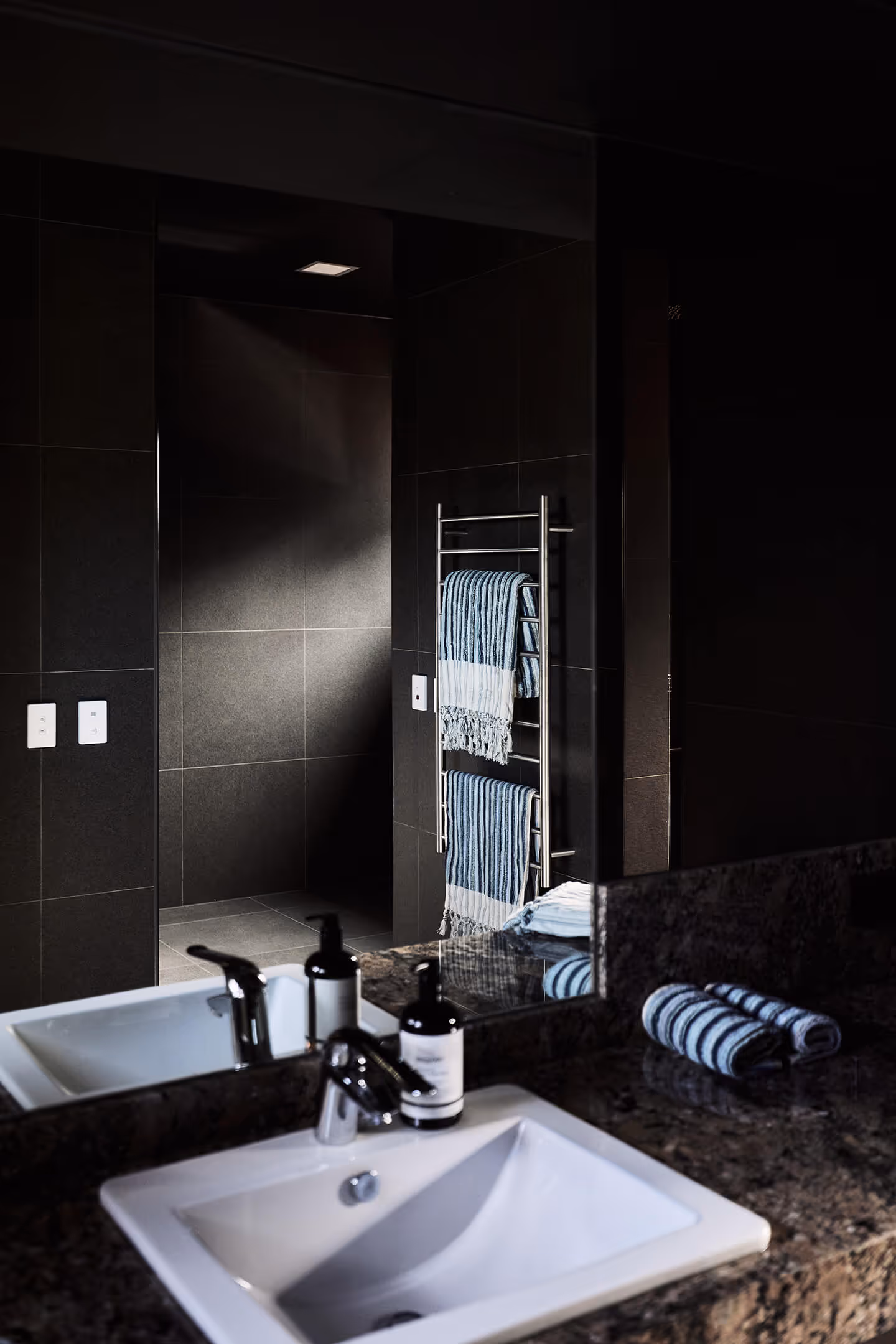Modern bathroom sink with faucet and soap bottles on granite countertop, towel rack with striped towels.
