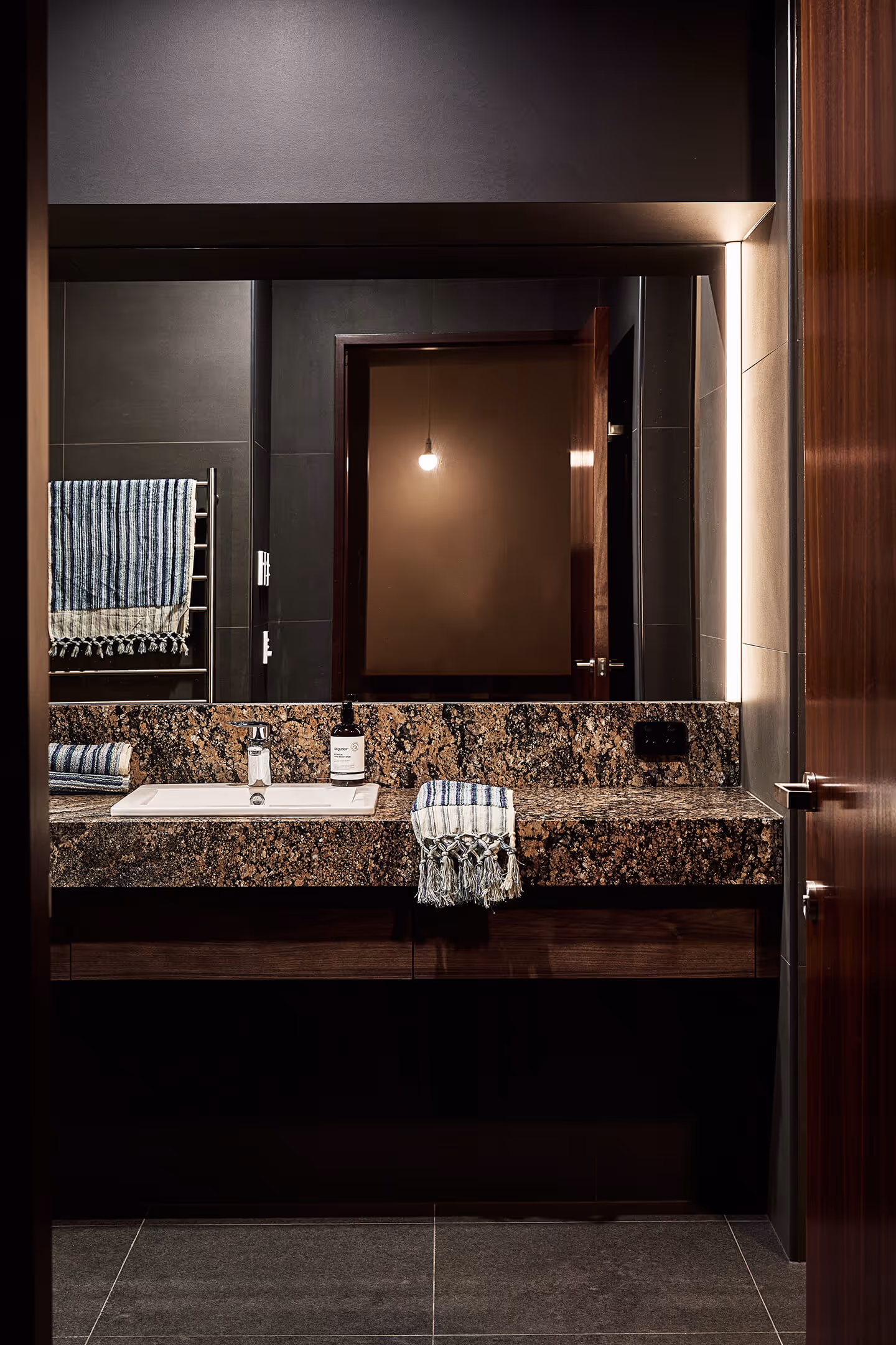Modern bathroom sink with granite countertop, striped towels, and a large mirror reflecting a lit bulb.