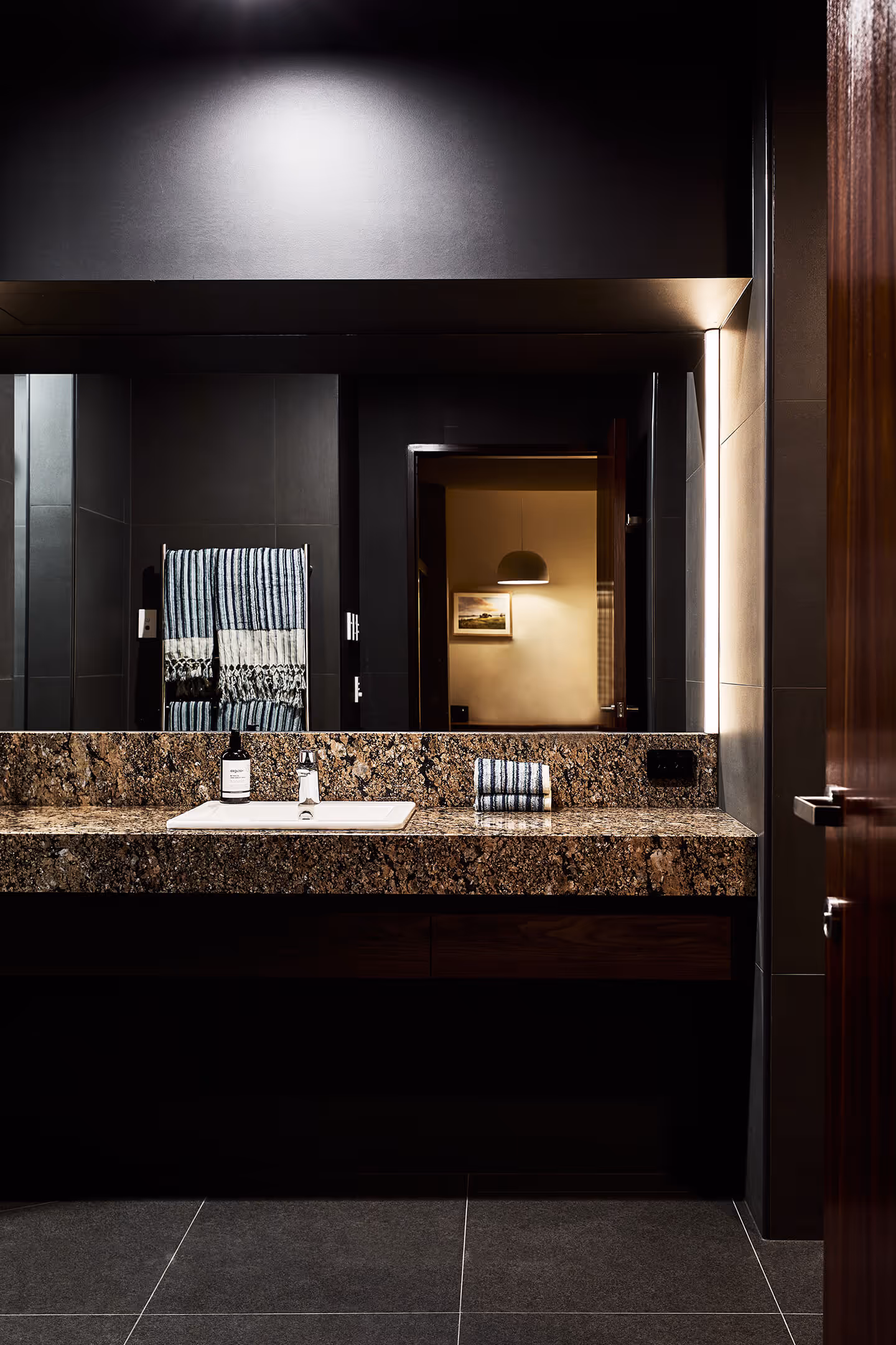 Modern bathroom with granite countertop, rectangular white sink, striped towels, and large mirror.