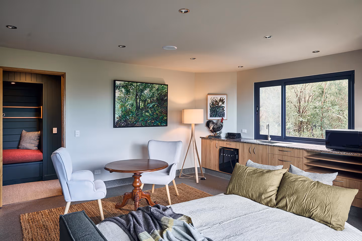 Cozy living space with a bed, two chairs around a wooden table, large window, and wood cabinetry.