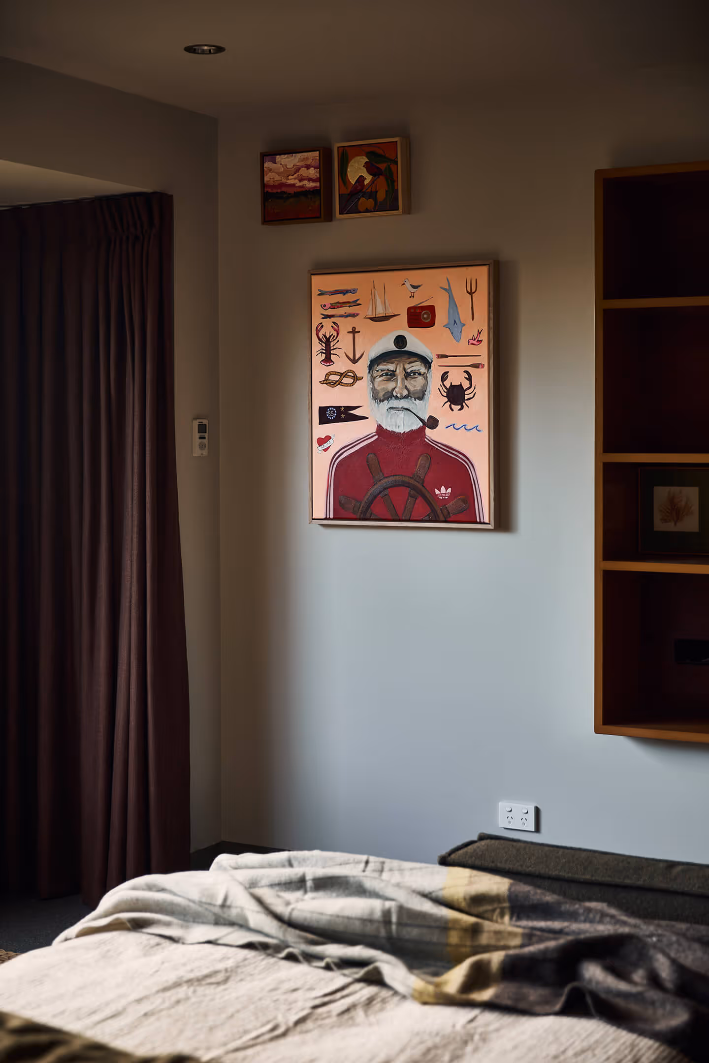 Room corner with nautical-themed painting of a captain and two small colorful paintings above.