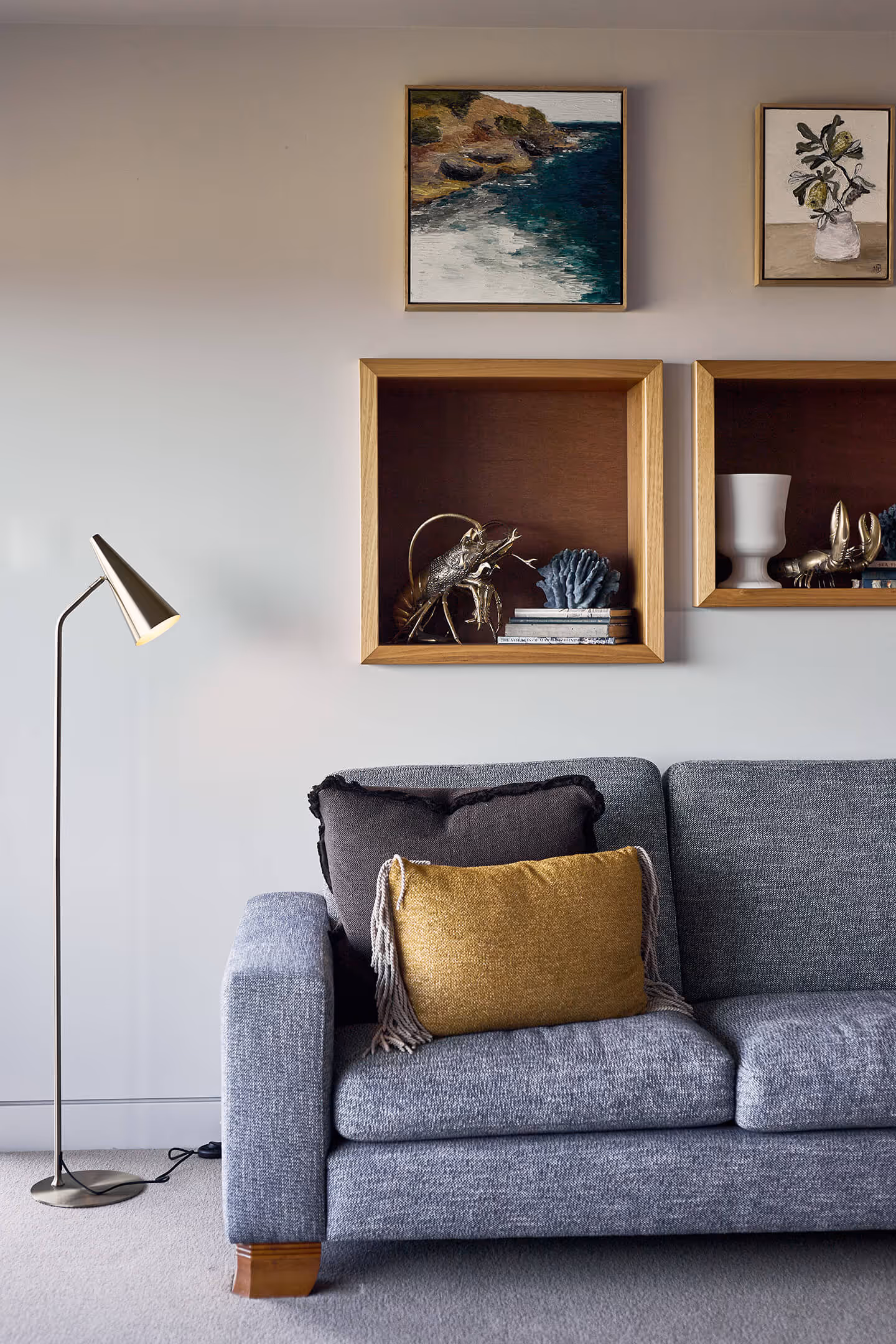 Gray sofa with black and mustard pillows, floor lamp, and wooden wall shelves with decor and art.