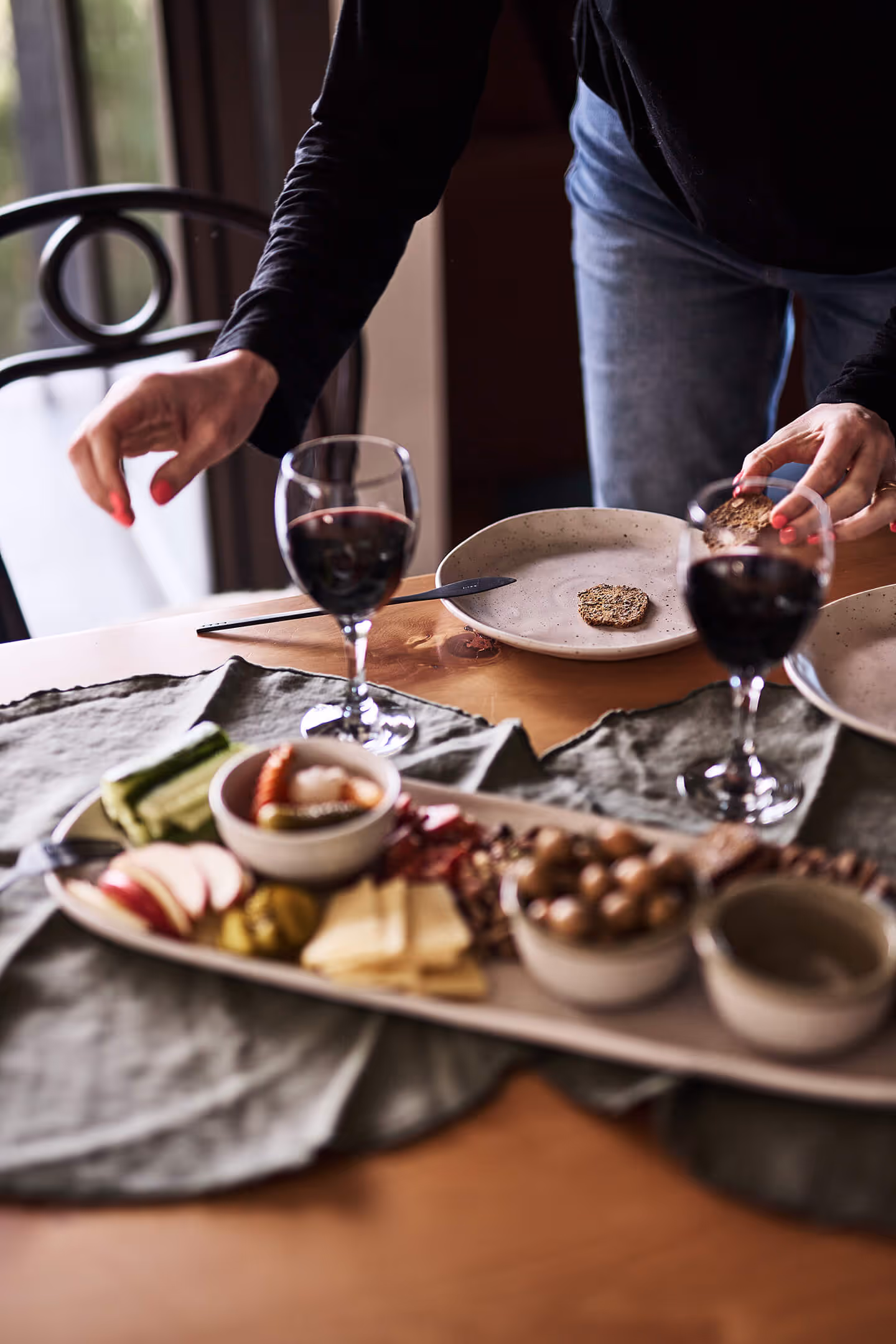 someone grabbing wine glasses full on a table spread of finger food