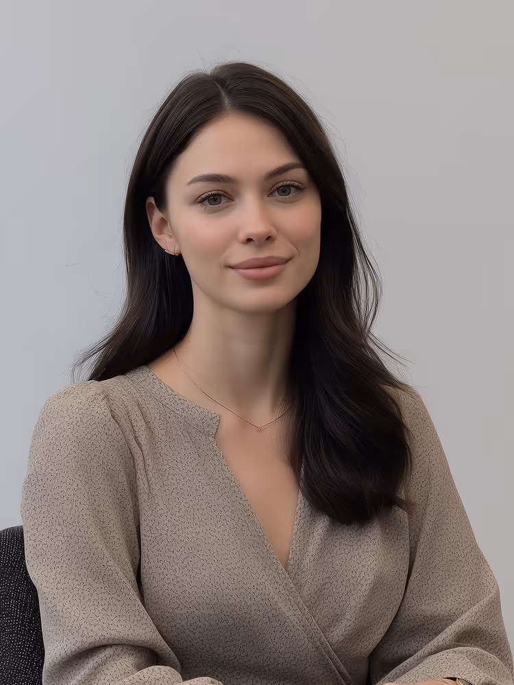Woman with long dark hair wearing a light brown blouse sitting against a plain light gray background.