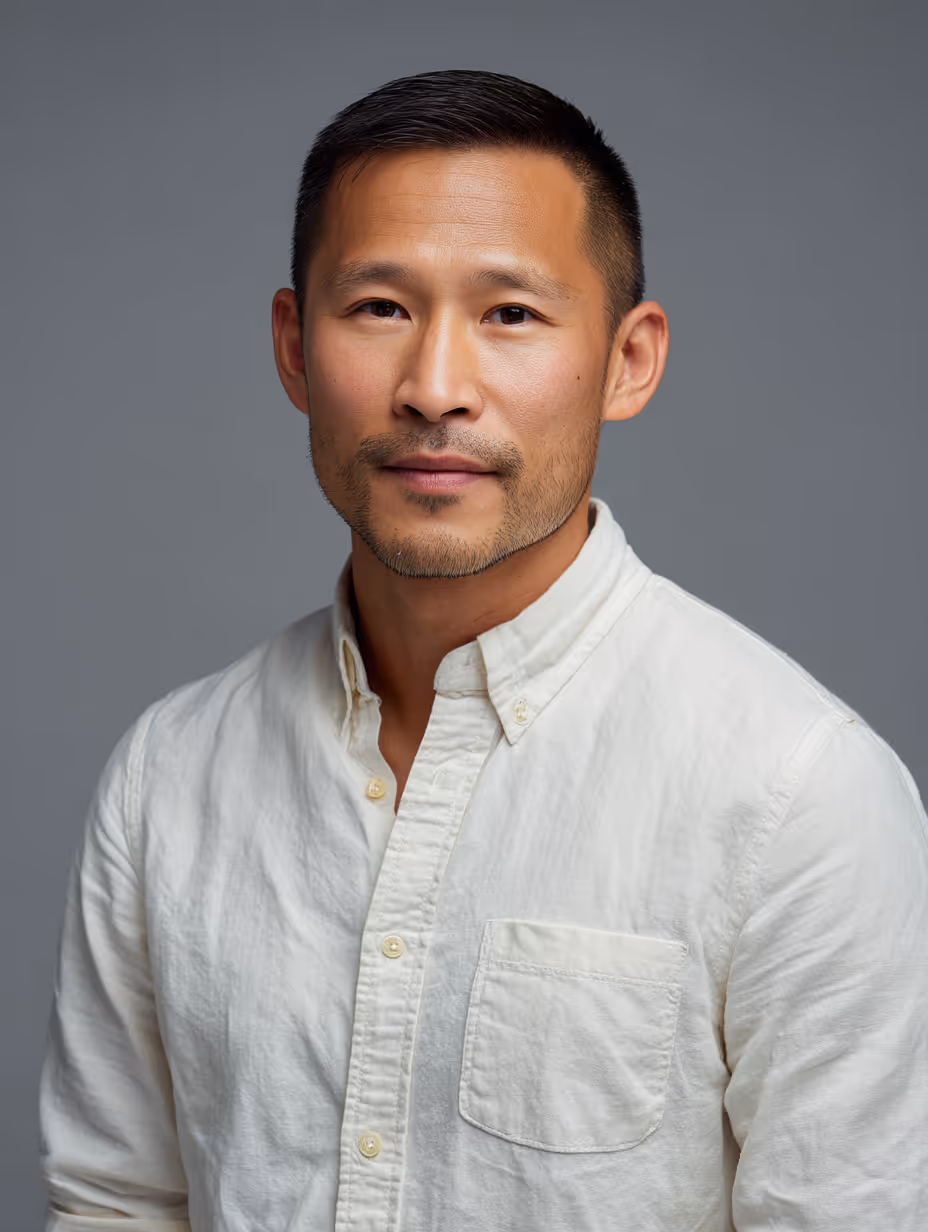 Portrait of a man with short dark hair and a trimmed beard wearing a white button-up shirt against a gray background.