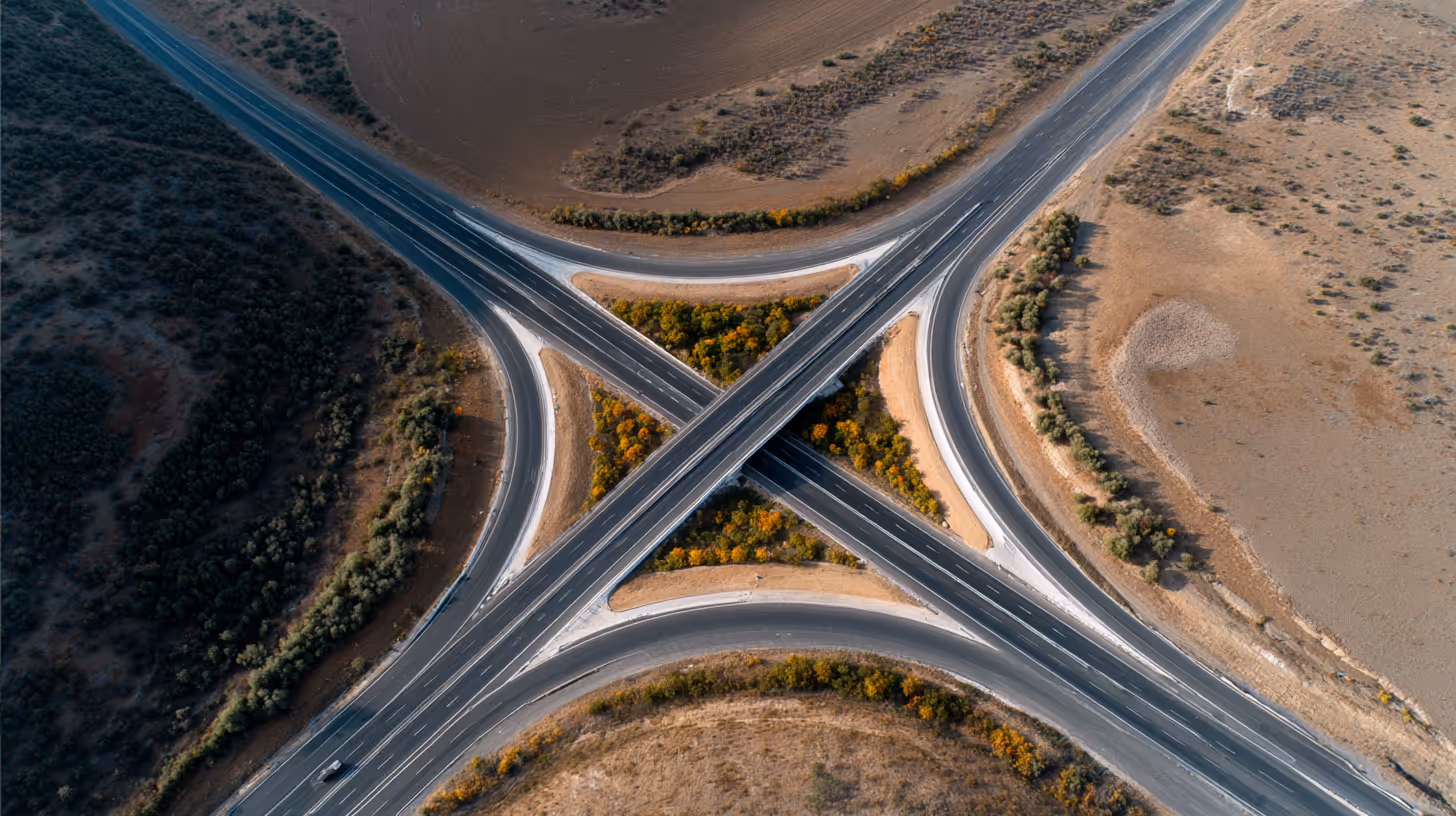 Aerial view of a highway overpass forming an X-shape with surrounding dry land and vegetation.