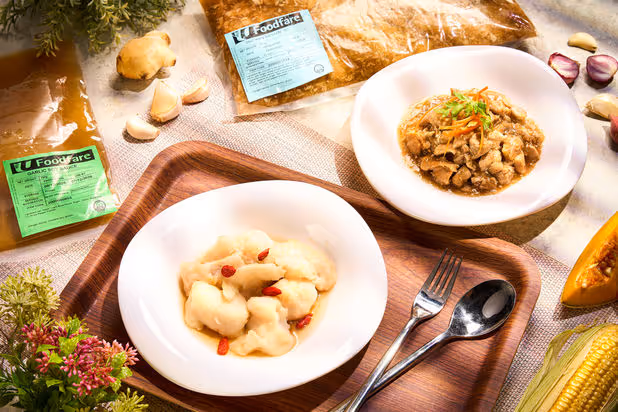 Two bowls of prepared meals on a tray beside packaged seasoning, garlic, corn, and pumpkin pieces.