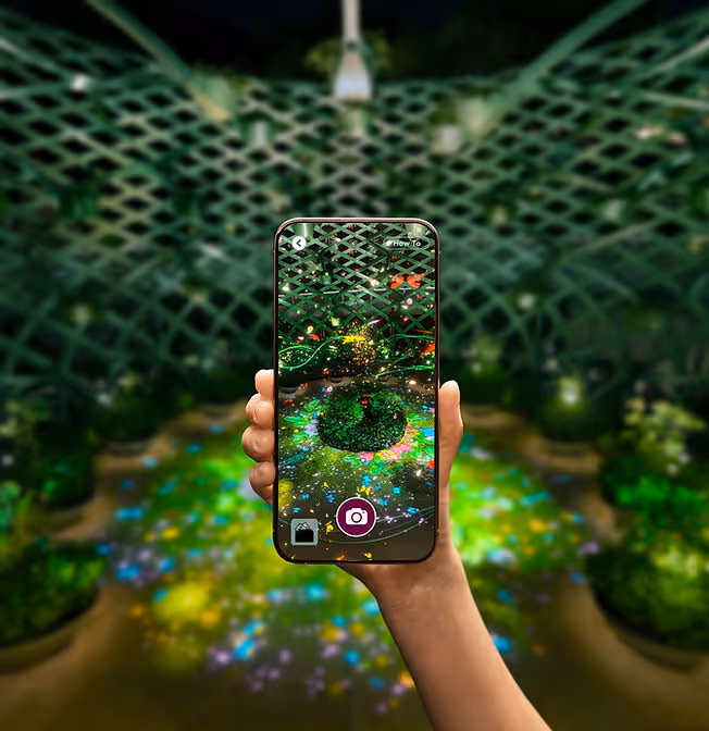 Hand holding a smartphone showing augmented reality flowers and lights in a garden at night.