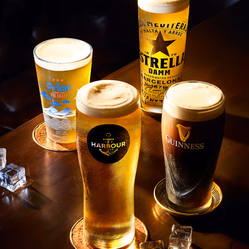 Four glasses with different beers on a wooden table illuminated by warm light.