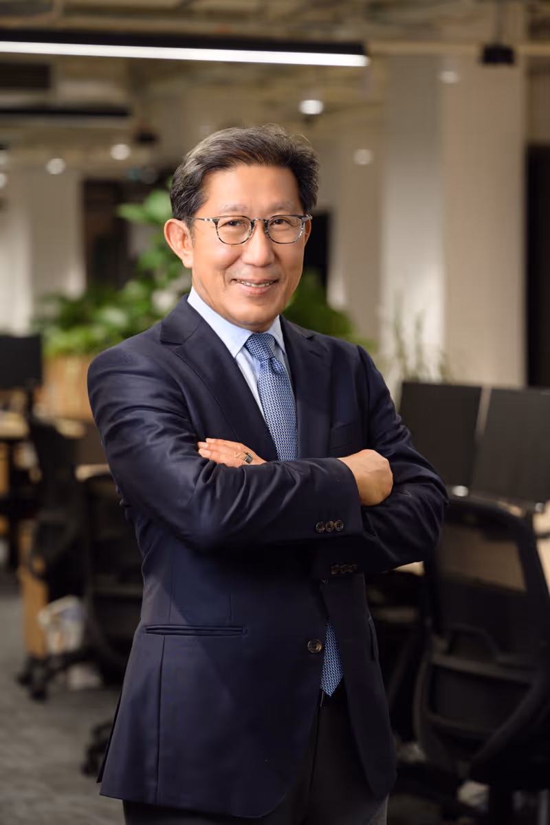 Smiling middle-aged man in glasses and suit standing with arms crossed in an office.