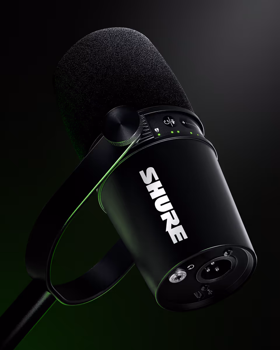 Close-up of a black Shure microphone with controls and a foam windscreen against a dark background.