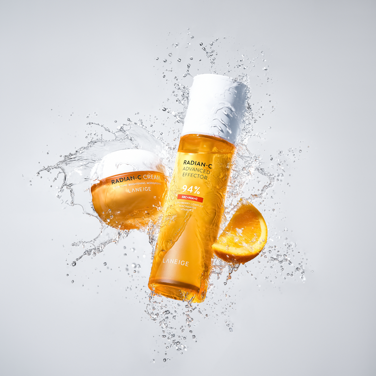 Laneige Radian-C skincare cream and effector bottles splashing with water and orange slice.