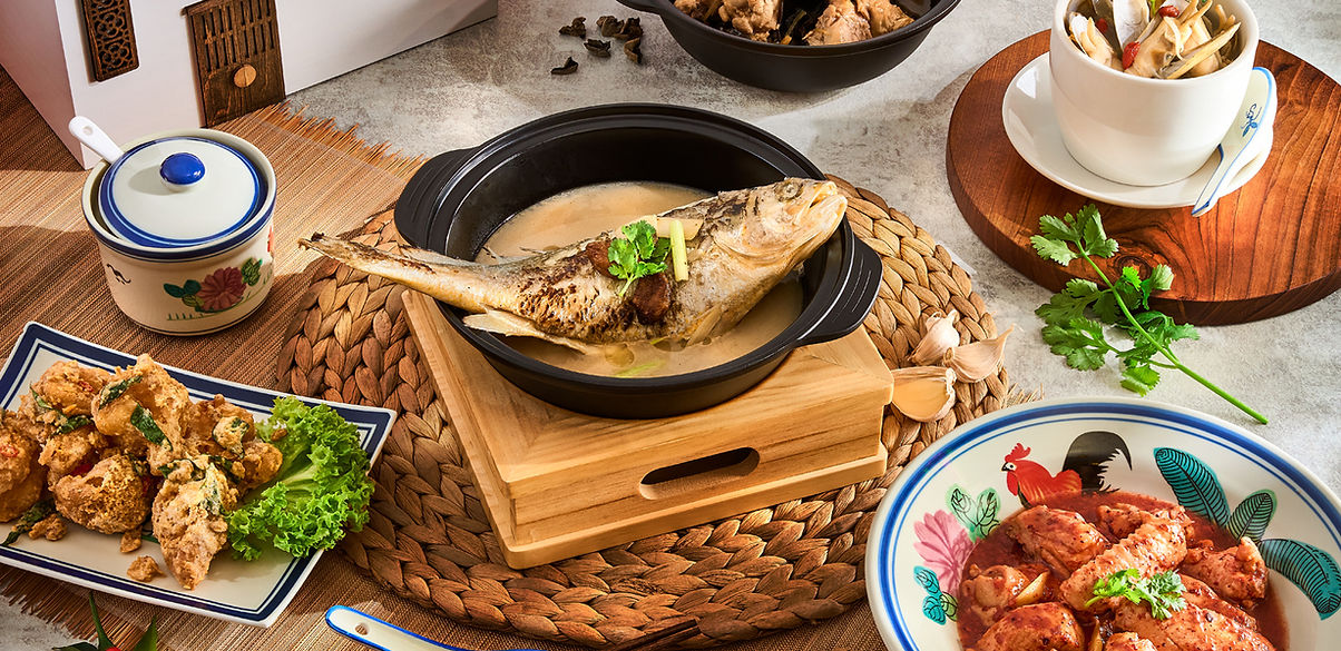 Table with various Asian dishes including a whole fish in broth, fried chicken pieces, and a bowl of spicy chicken wings.