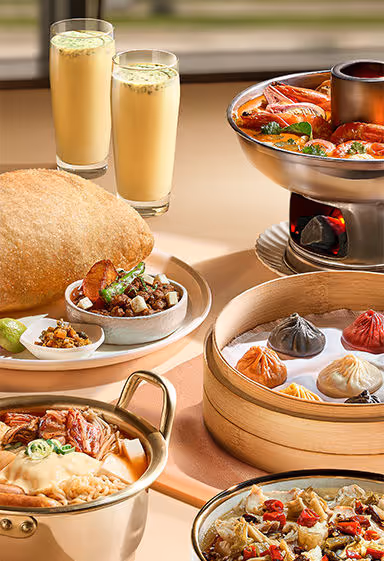 Table with Asian dishes including dumplings, hot pot seafood, fried snacks, and two glasses of yellow drinks.