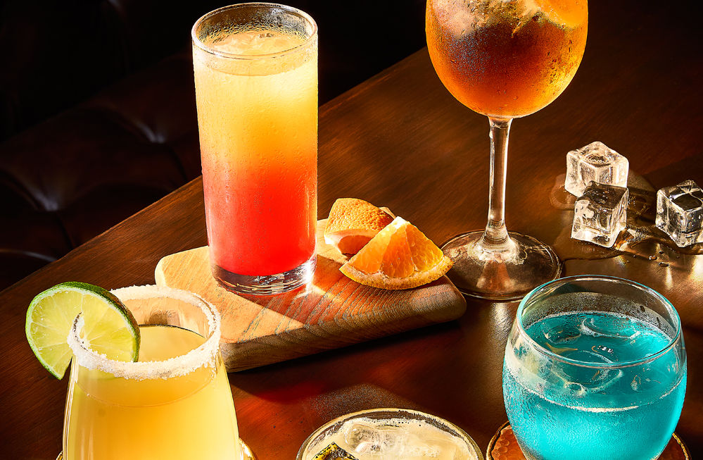 Table with colorful cocktails including a margarita with lime and salted rim, and others with ice and fruit.