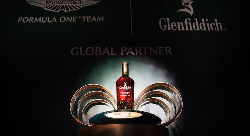 Glenfiddich whiskey bottle displayed on a curved metal stand with Aston Martin Formula One branding.
