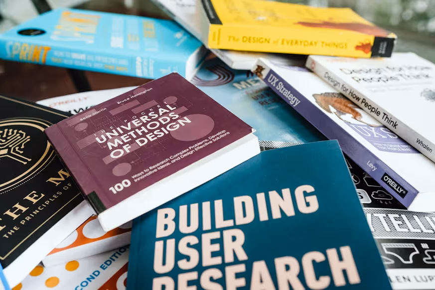 Stack of design and user research books on a table including Universal Methods of Design and Building User Research.