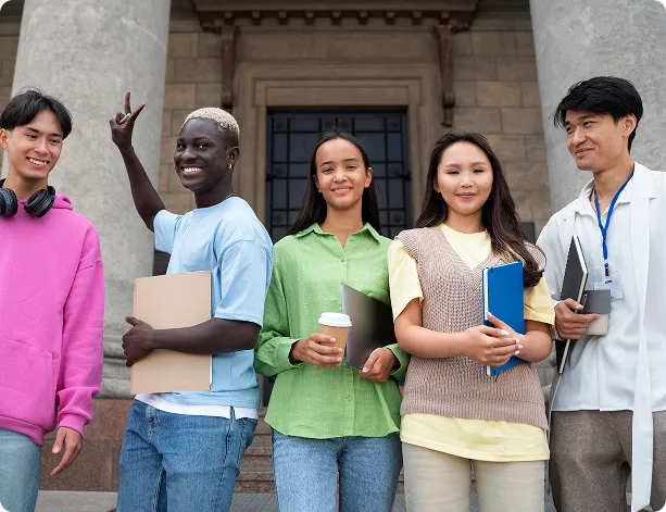 Group of five diverse young students standing outside a building with books and laptops.