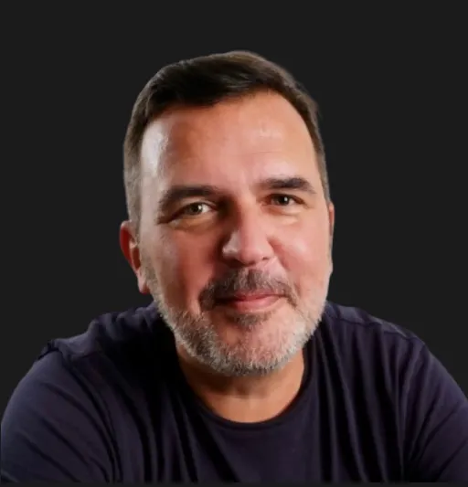 Smiling middle-aged man with short dark hair and beard wearing a dark shirt, black background.