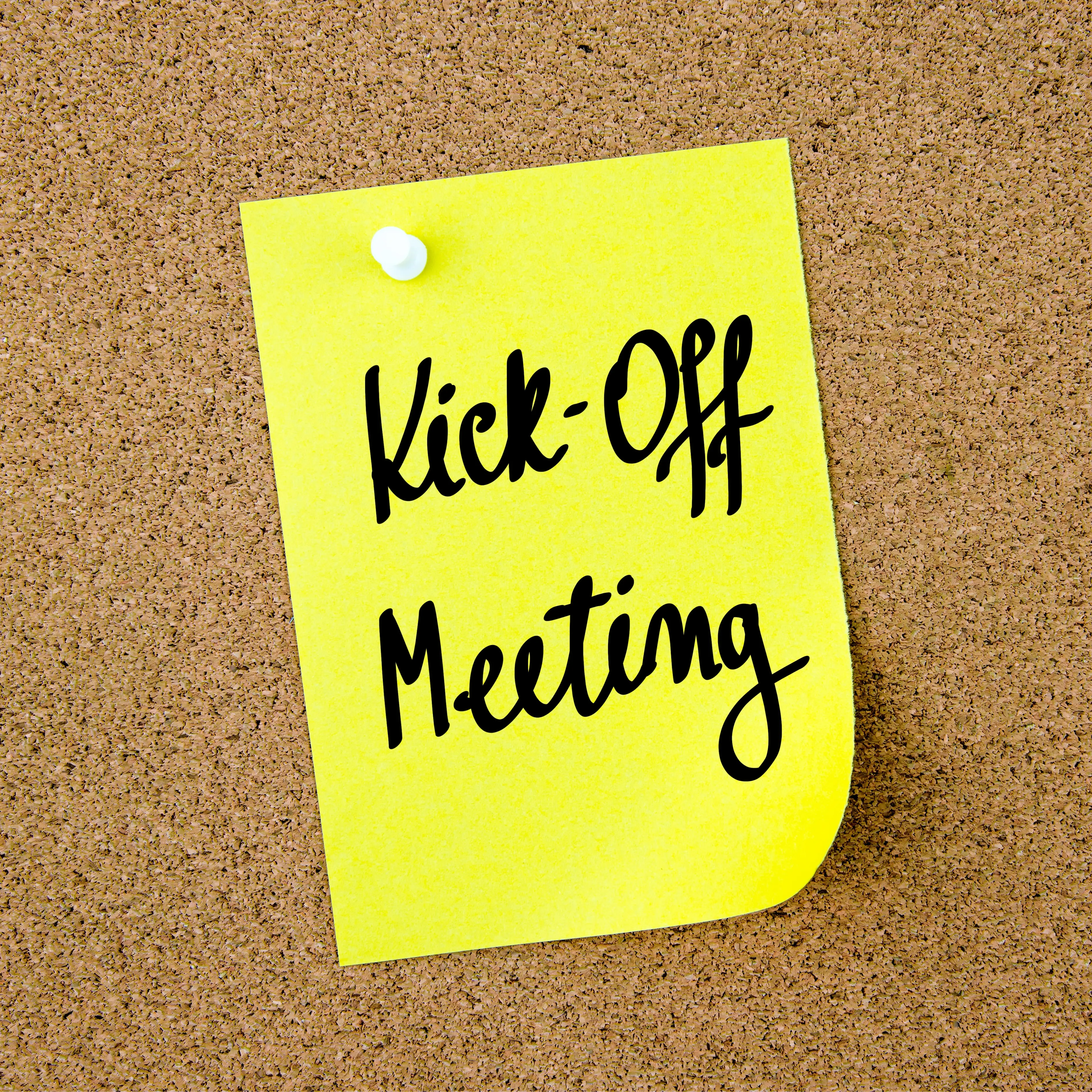 Yellow sticky note pinned on cork board with handwritten text: Kick-Off Meeting.