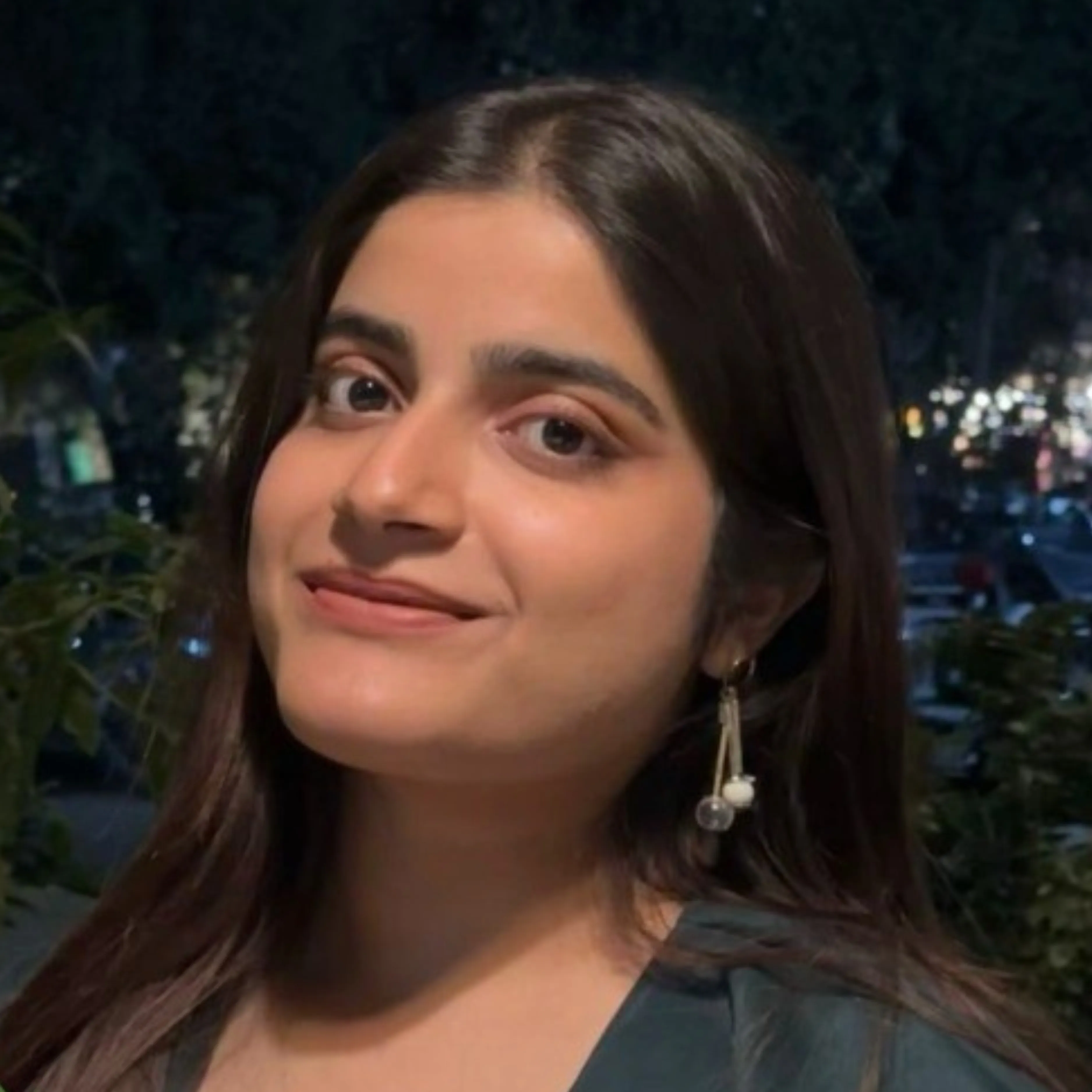 Young woman with long dark hair smiling softly at night with dangling pearl earrings.