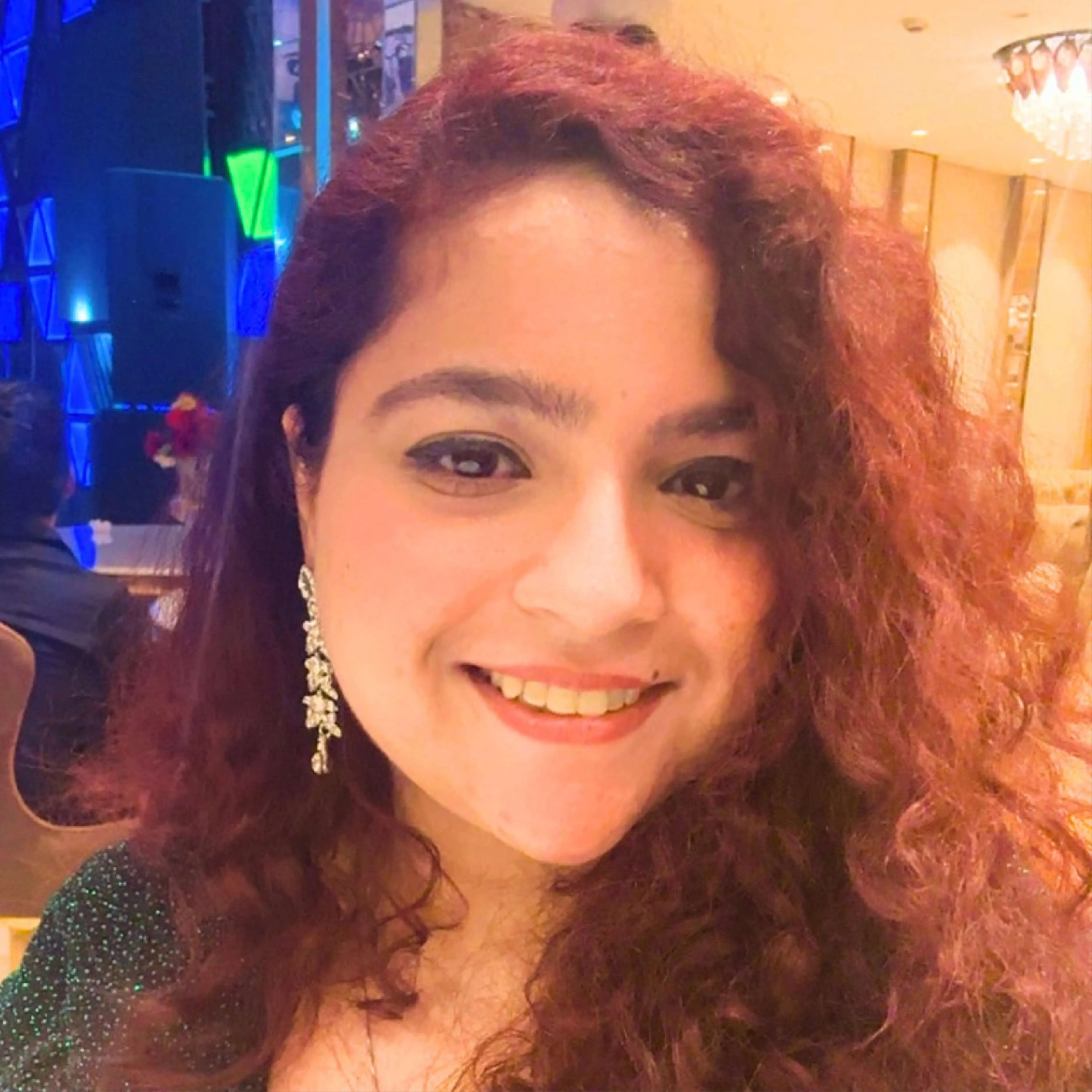 Smiling woman with curly reddish hair and long decorative earrings at an indoor event.