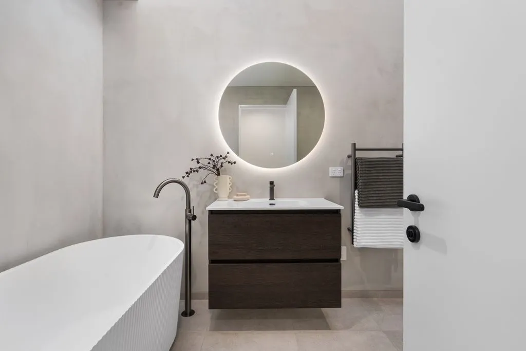 Bathroom with dark wood floating vanity and round mirror with LED lighting