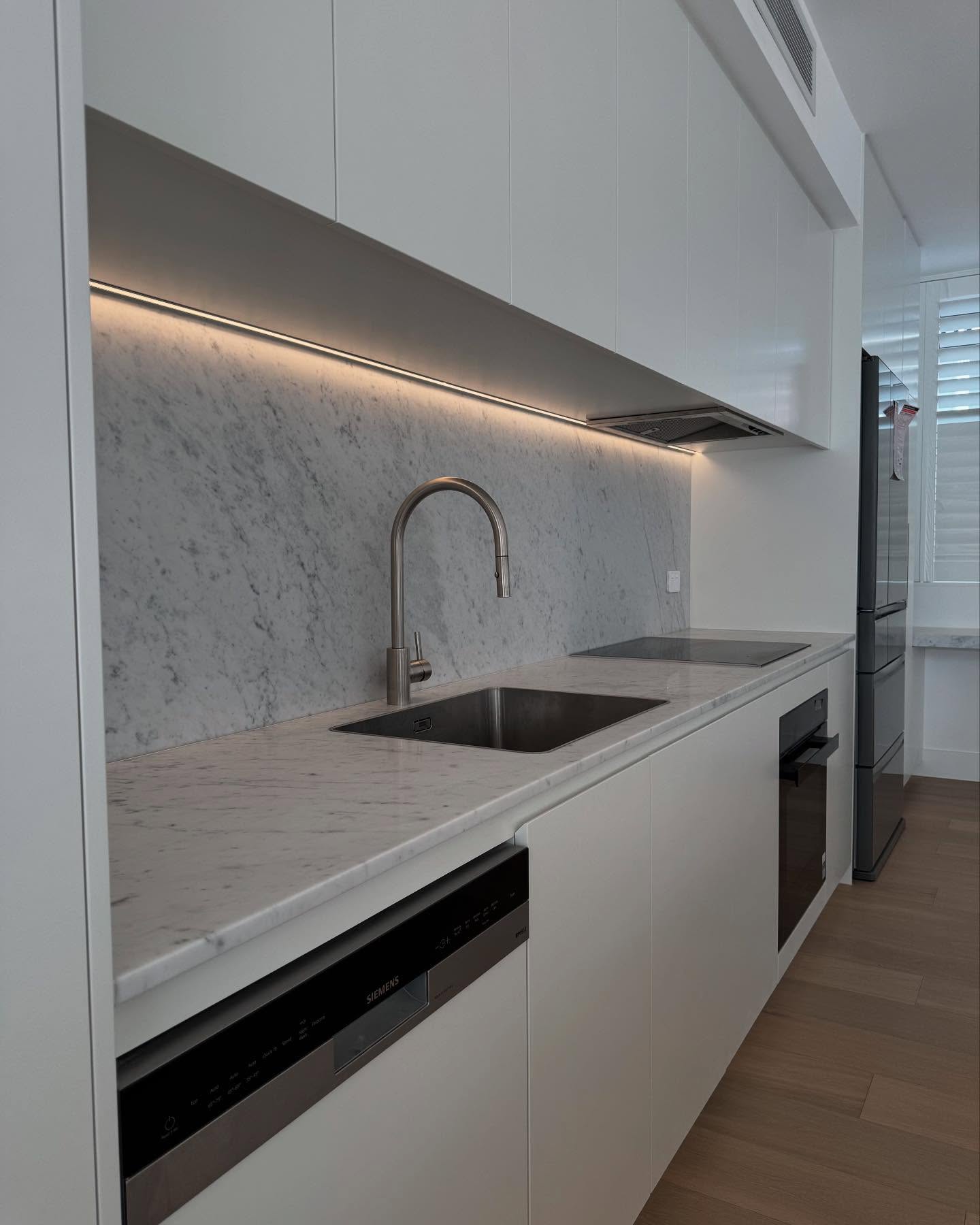 Undermount sink, curved tap and full-height stone splashback.