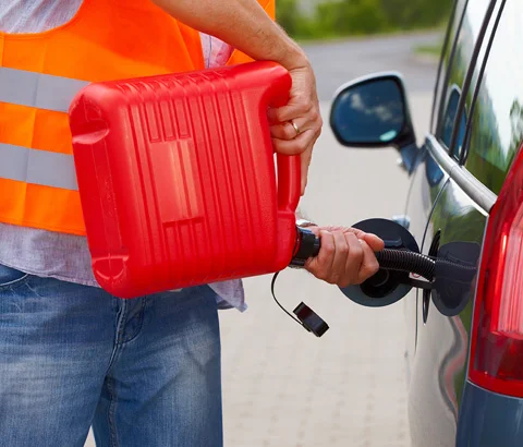 Roadside worker pouring fuel from a red container into a car.