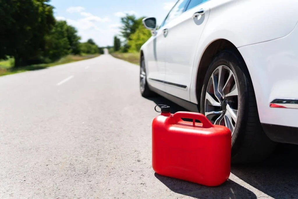 Red fuel container beside a car stopped on a road.