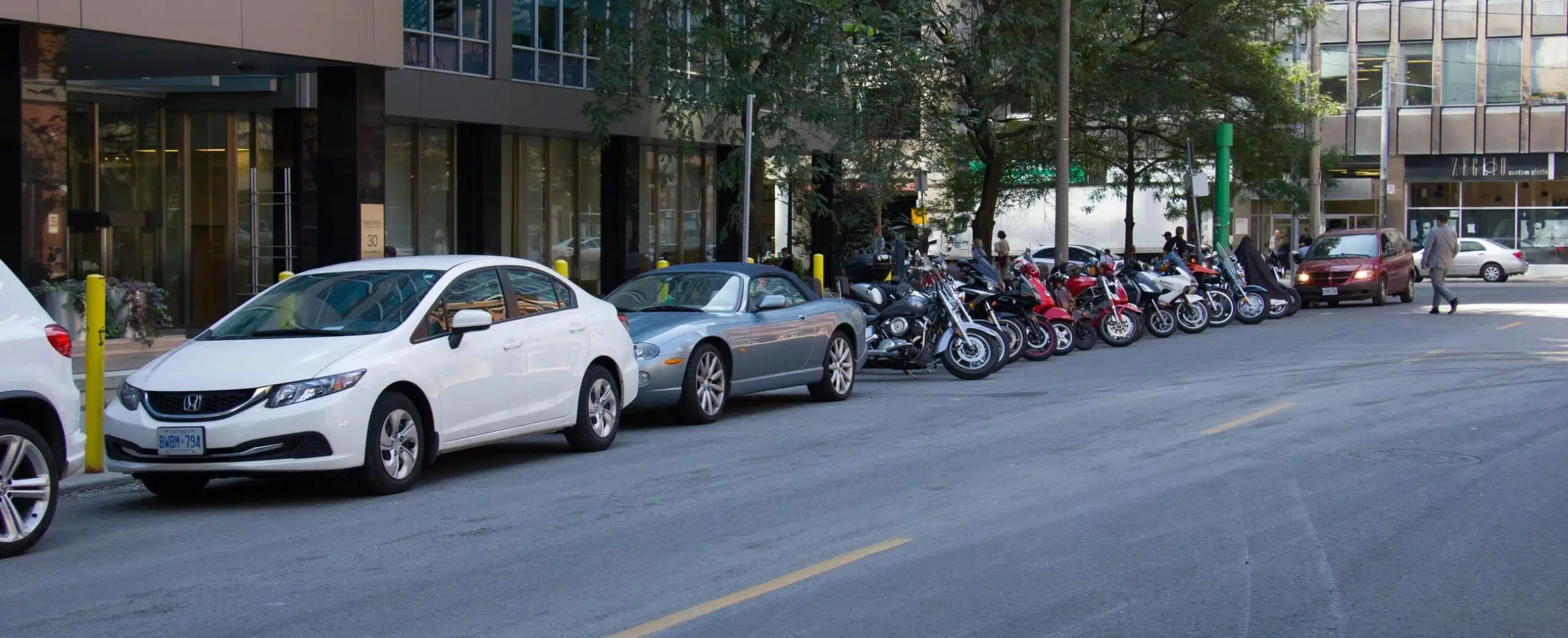 Parked cars and motorcycles along a downtown Toronto street.