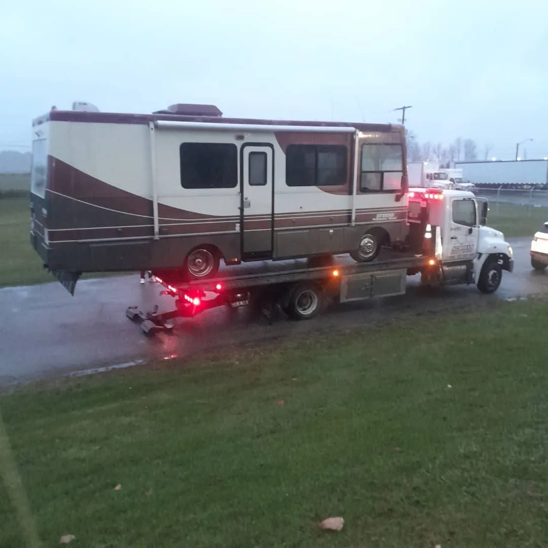 Motorhome on a flatbed tow truck beside a road.