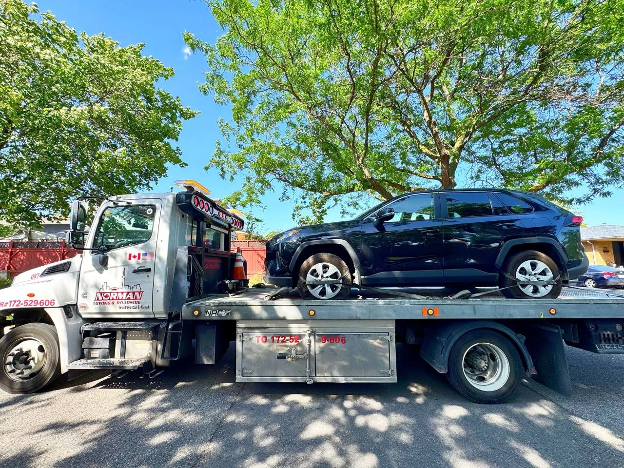 Norman Towing flatbed with a sedan on a suburban Toronto street