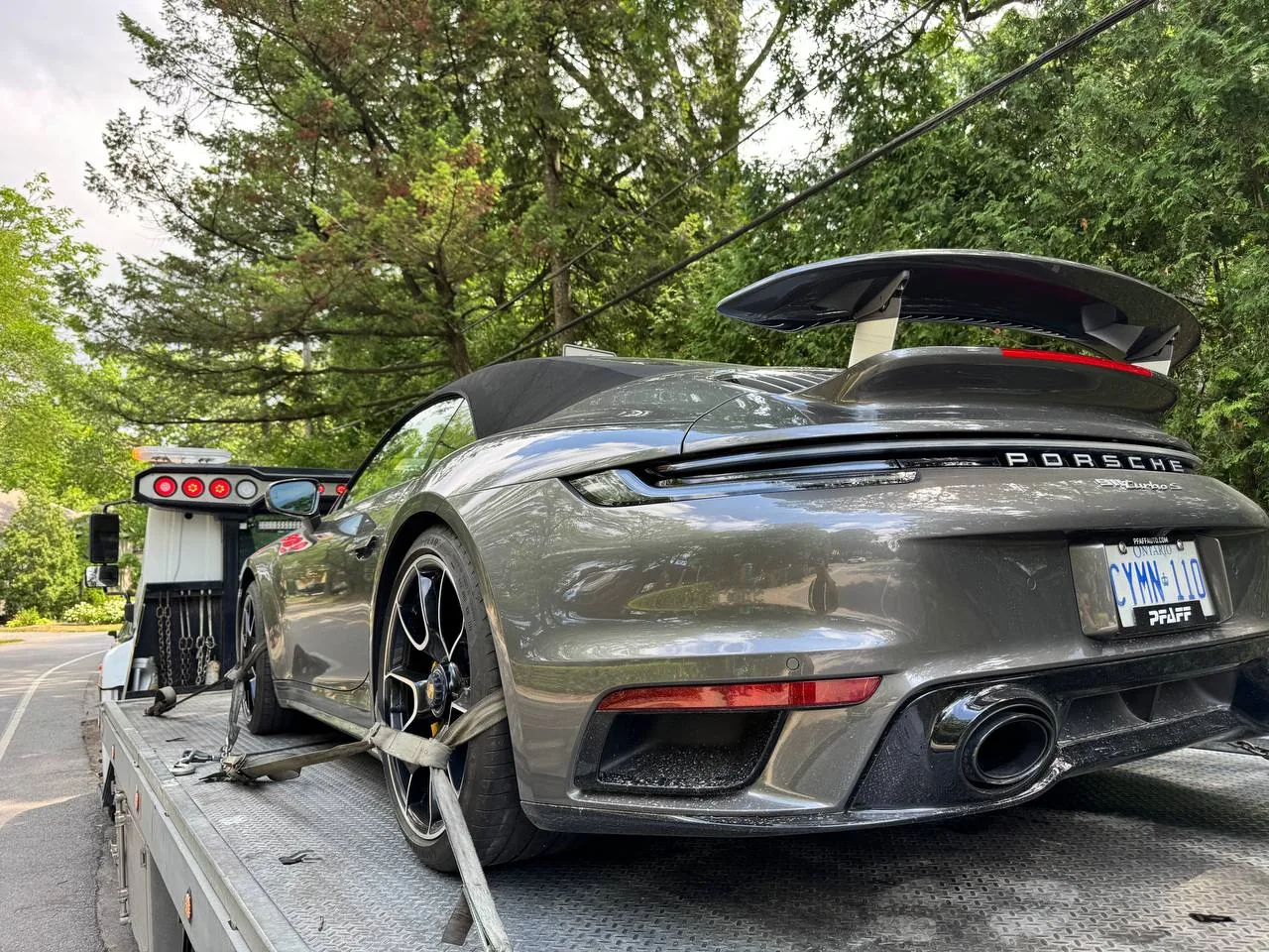Rear view of a Porsche 911 secured with wheel straps on a flatbed.