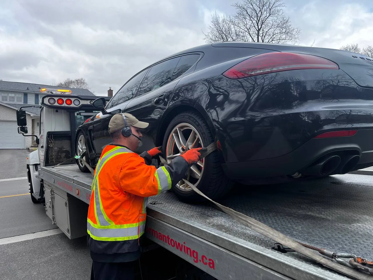 Tow operator securing a wheel strap on a Porsche carried by a flatbed.