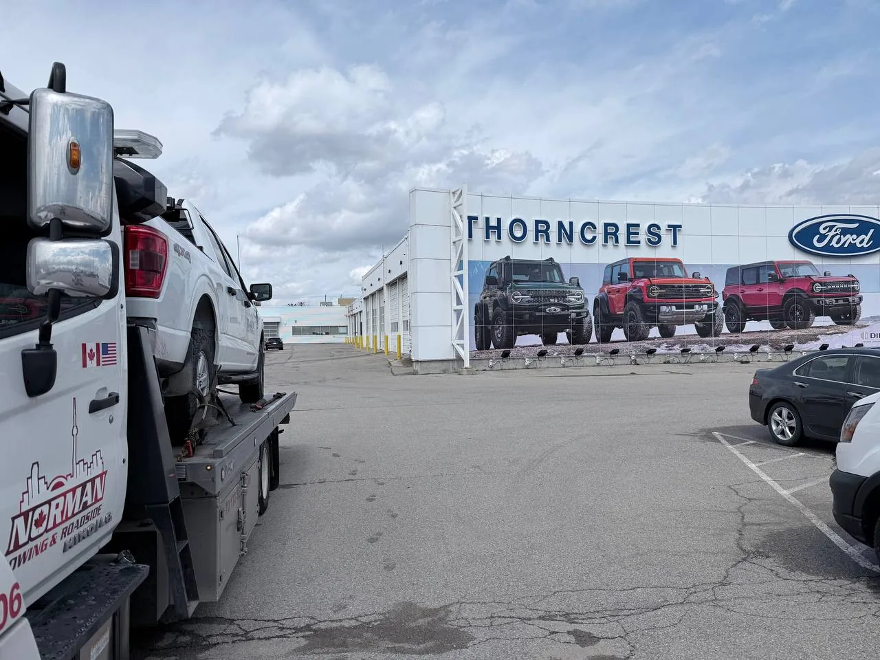 Norman Towing flatbed carrying a vehicle at a Ford dealership.