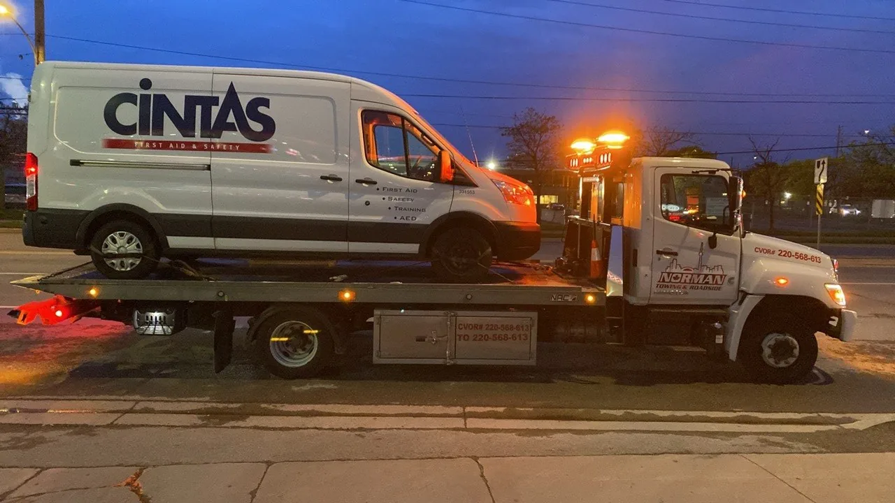 Cintas service van on a Norman Towing flatbed at dusk.