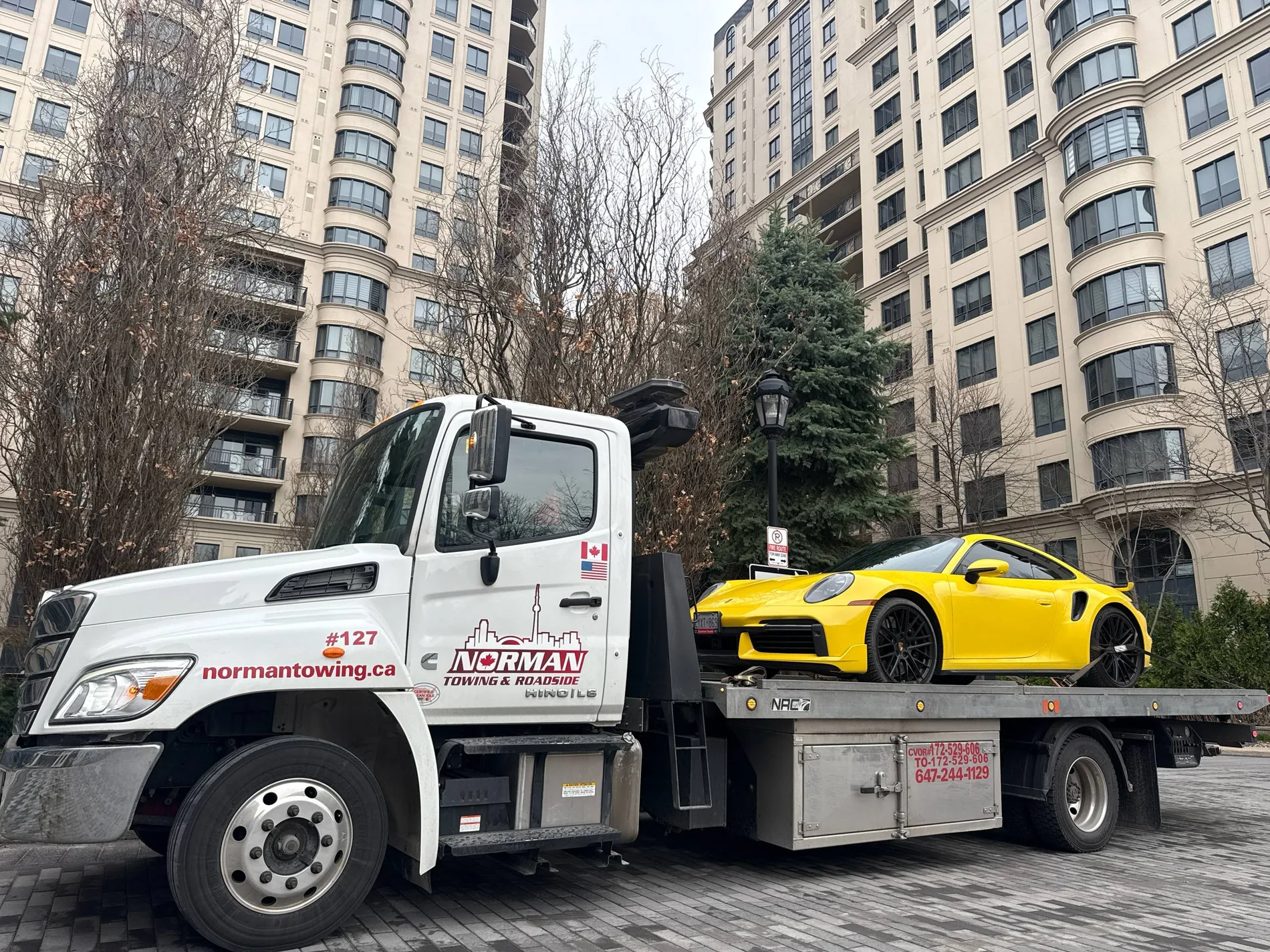 Yellow Porsche on a Norman Towing flatbed outside condominium buildings.