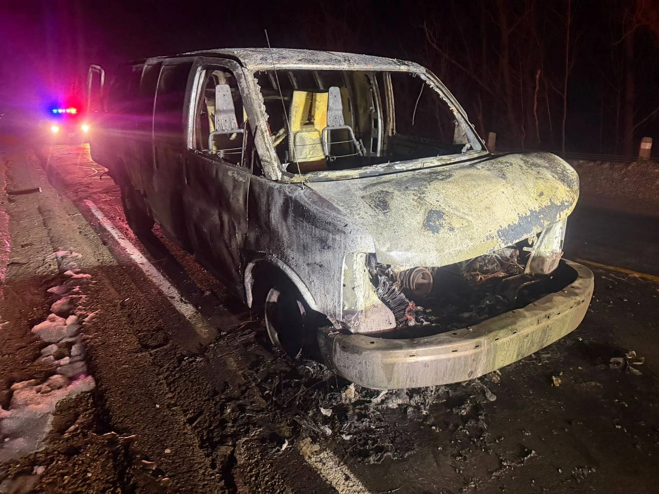 Burned-out van beside emergency lights on a road at night.