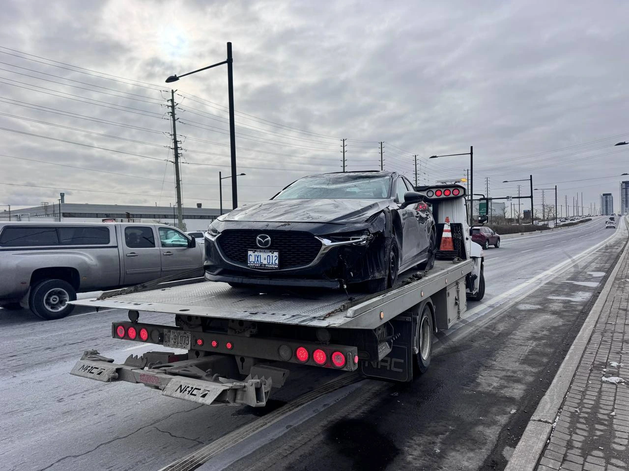 Collision-damaged Mazda3 secured on a flatbed beside a snowy road.