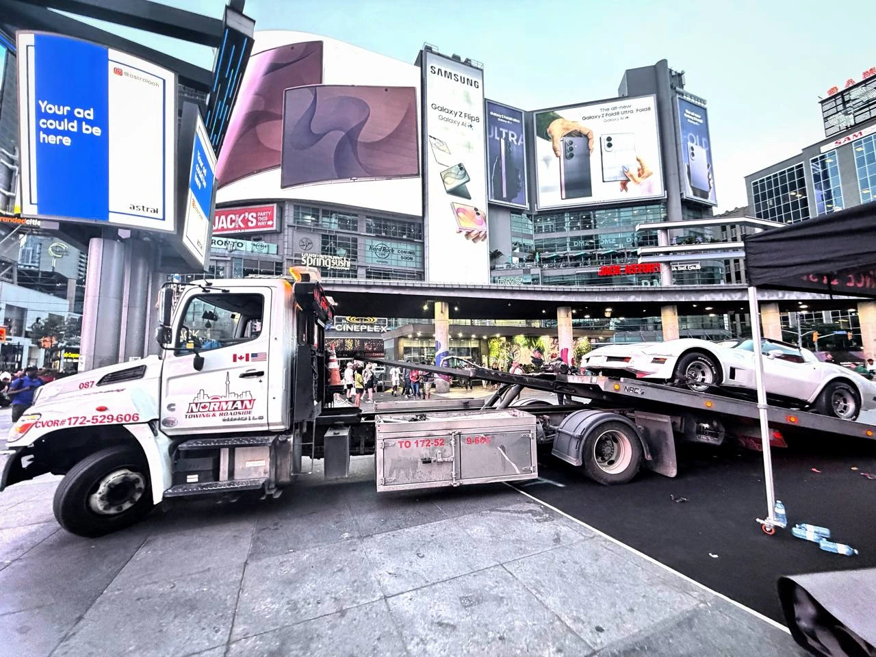 Norman Towing flatbed carrying a white classic Corvette at Yonge-Dundas Square.