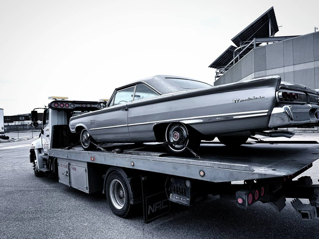 Silver Cadillac convertible secured on a flatbed tow truck.
