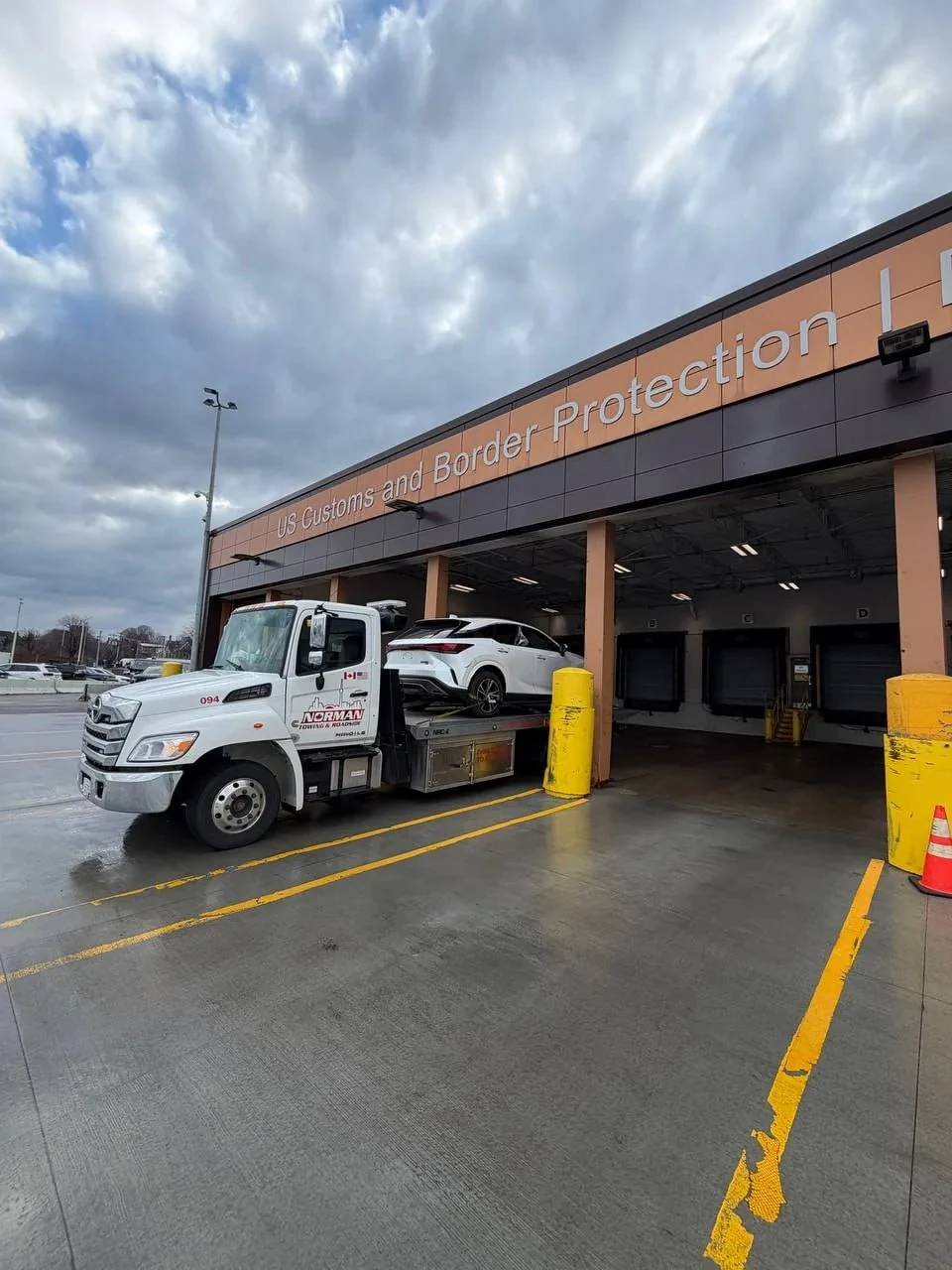 Flatbed tow truck carrying a white car outside an inspection building.