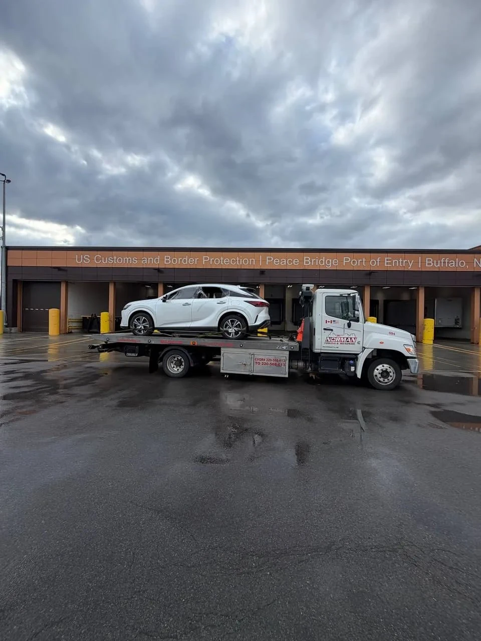 White car secured on a flatbed tow truck beside an inspection building.