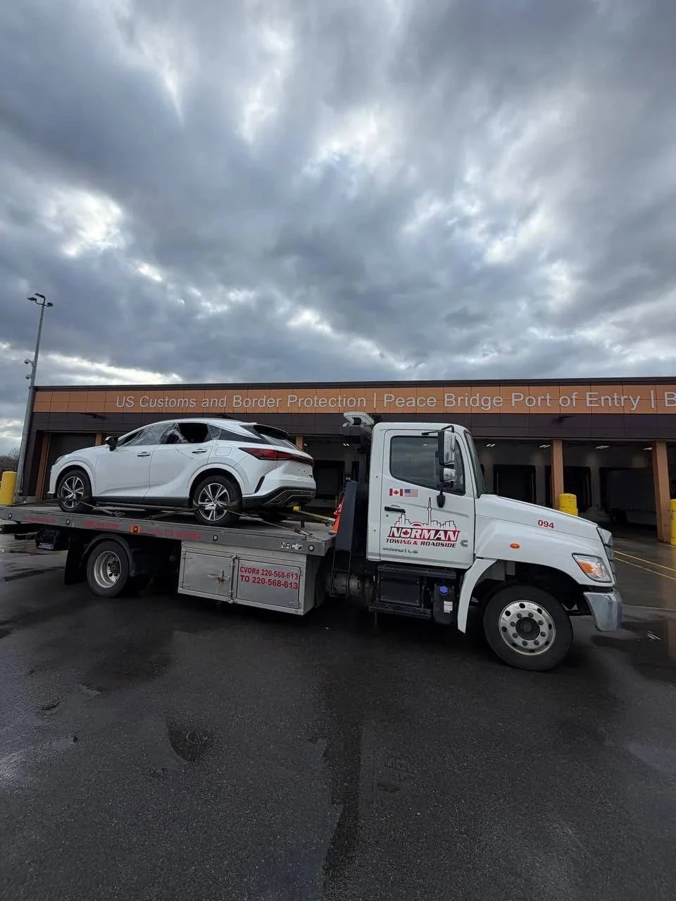 White sedan on a Norman Towing flatbed outside an inspection building.