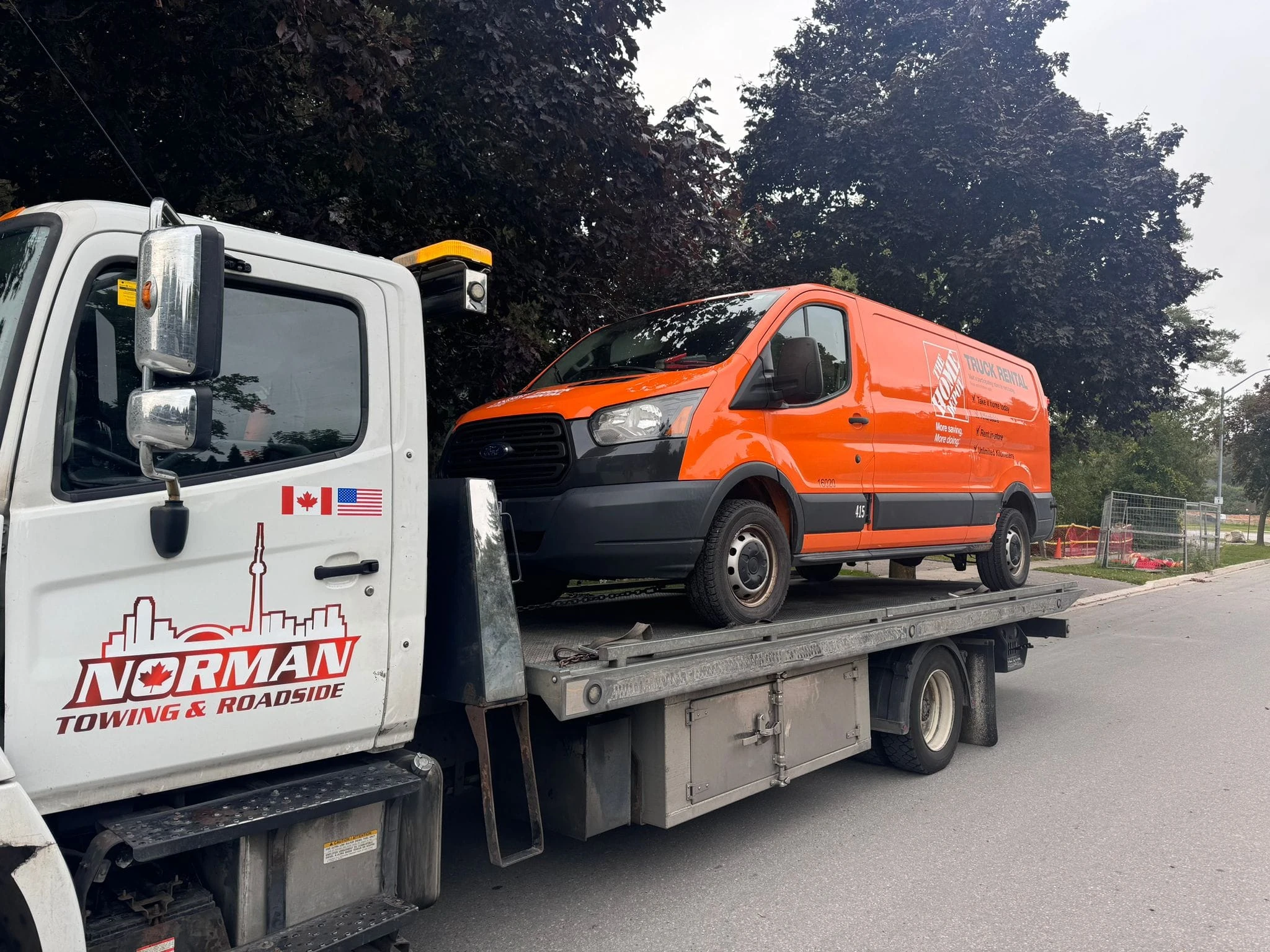 Orange commercial van carried on a Norman Towing flatbed truck.