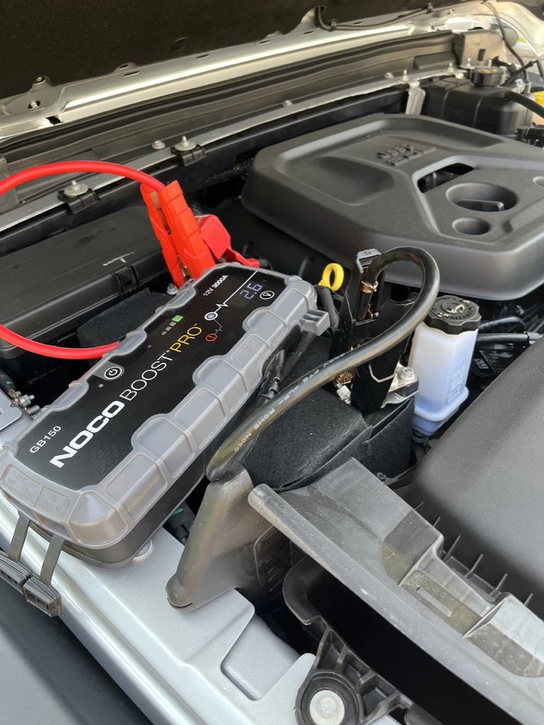 Portable jump starter connected to a vehicle battery under an open hood.